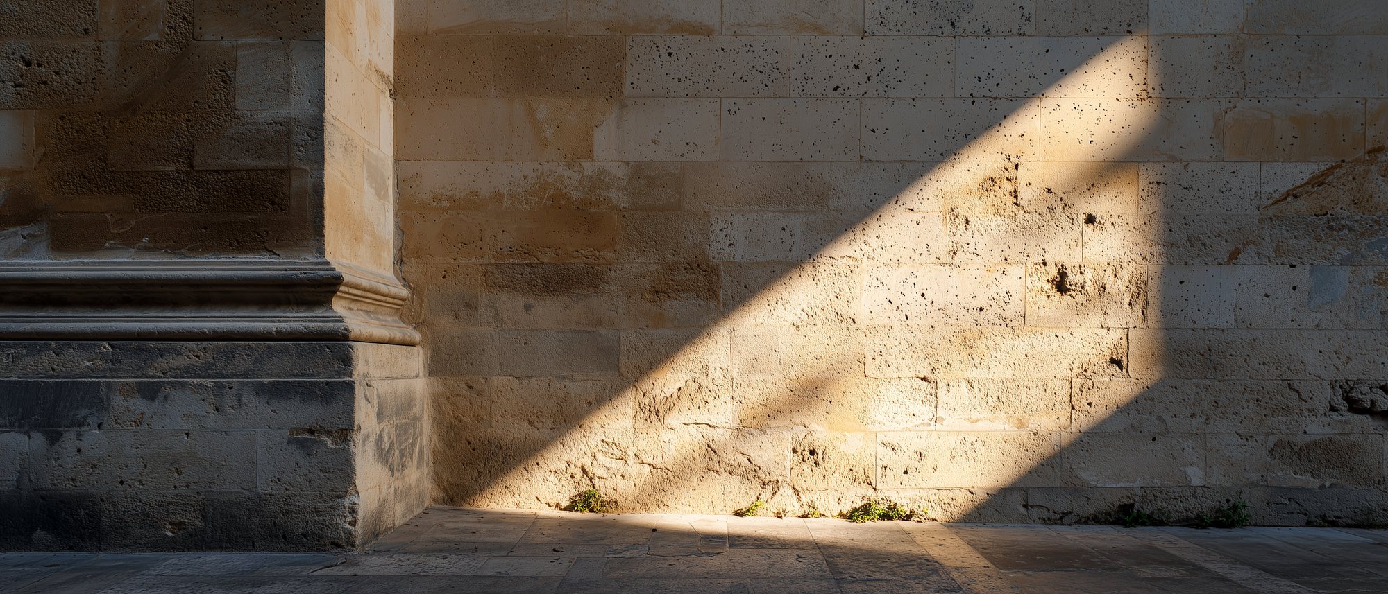 Un muro di pietra leccese con l'ombra netta di uno stipite che lo attraversa in diagonale